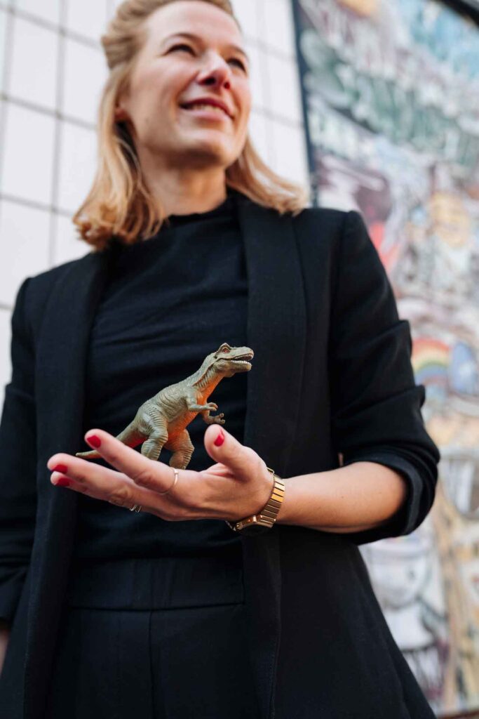 Das Bild zeigt, wie Britta Cornelißen einen Spielzeug-Dinosaurier in der Hand hält und lächelt.